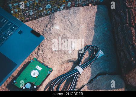 Laptop-ethernet-Kabel und Festplatte sitzen während der goldenen Stunde auf einem Felsen draußen Stockfoto