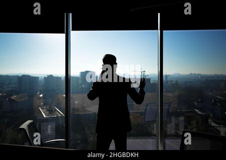 Silhouette eines Geschäftsmannes in einem modernen Büro auf dem Hintergrund des Fensters, eines Mannes, der am Telefon spricht Stockfoto