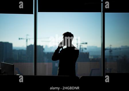 Silhouette eines Geschäftsmannes in einem modernen Büro auf dem Hintergrund des Fensters, eines Mannes, der am Telefon spricht Stockfoto