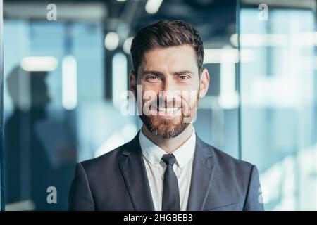 Nahaufnahme eines Geschäftsmannes mit Bart, der die Kamera anschaut und lächelt, eines Mannes im modernen Büro Stockfoto