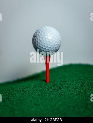 Sauberes Bild eines weißen Golfballs, der auf einem roten Golf-T-Shirt aus Holz sitzt. Grasboden mit weißem Hintergrund Stockfoto