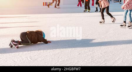 Weich, selektive Focus.The Kind fiel auf die Eisbahn während Skating.Adorable kleines Kind in Winterkleidung mit Schutzmaßnahmen Eislaufen auf Eisbahn.Funny Moment Stockfoto