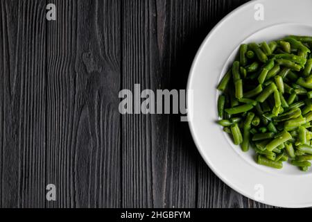 Servieren von grünen Bohnen weißen Teller auf dunklem Holzbrett, Low-Key-Foto mit Kopierplatz. Stockfoto