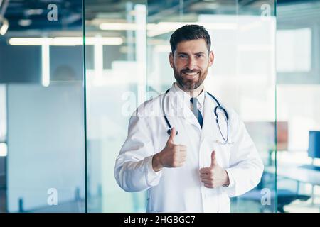 Erfolgreicher männlicher Arzt lächelt und schaut in der Klinik auf die Kamera Stockfoto