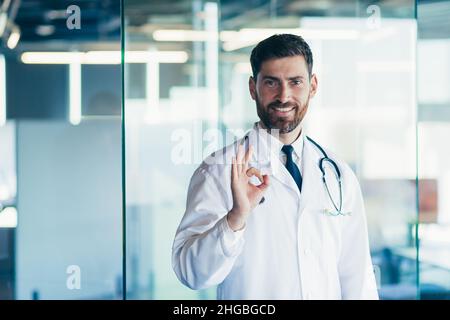 Erfolgreicher männlicher Arzt lächelt und schaut in der Klinik auf die Kamera Stockfoto