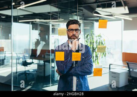 Der junge bärtige Executive Manager Businessman CEO schreibt seine Strategieideen auf Notizen auf einer Tafel und leitet die Präsentation eines Geschäftsplans Stockfoto