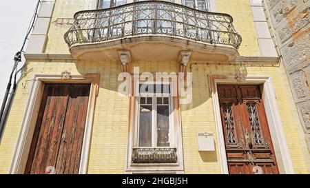 Fassade mit gelben Kacheln, neoklassizistisches Stadthaus, geplatzte Holztüren, Metallgeländer, Balkon, geschlossene Fenster. Tavira-Portugal-067 Stockfoto