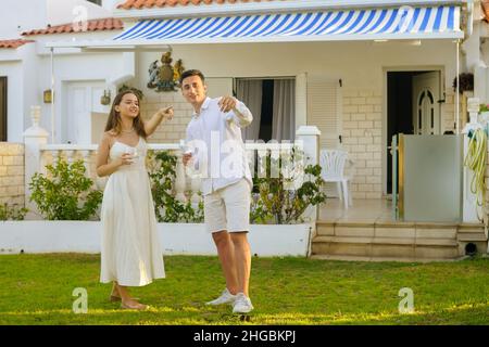 Schönes Mädchen in einem weißen Kleid auf einem Date mit einem Mann in Weiß. Ein Paar feiert den Kauf eines Hauses am Meer. Schönes Paar trinkt Wein in der Nähe der h Stockfoto