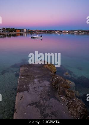 Dock, Kai auf der Insel Vir, Kroatien früh am Morgen. Dock und Gummiboot mit Blick auf den wunderschönen lila und rosa Himmel über der Adria. Stockfoto