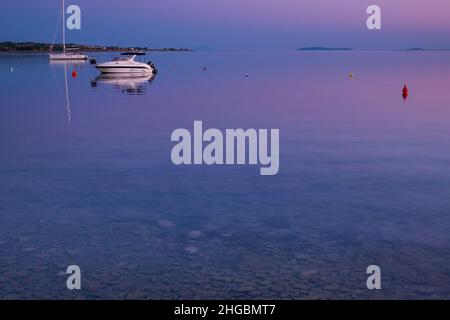 Meerblick auf der Insel Vir, Kroatien am frühen Morgen. Zwei weiße Boote mit Blick auf den wunderschönen lila und rosa Himmel über der Adria. Stockfoto