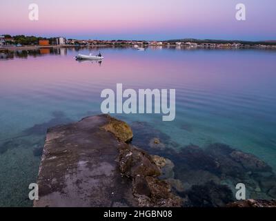 Dock, Kai auf der Insel Vir, Kroatien früh am Morgen. Dock und Gummiboot mit Blick auf den wunderschönen lila und rosa Himmel über der Adria. Stockfoto