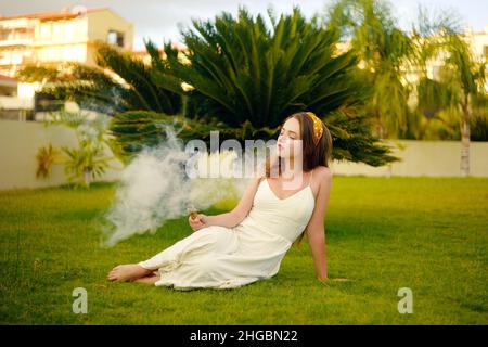 Eine Vape-Frau im Urlaub, unter einer Palme. Ruhe, Rauchen, Nikotin, Genuss, Gefahr. Flüssigkeit abdampfen. Dampfende THC e Zigarette. Stockfoto