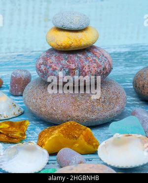 Auf dem Tisch liegen Meeressteinchen und Muscheln. Eine Pyramide aus Seesteinen auf blauem Hintergrund. Stockfoto