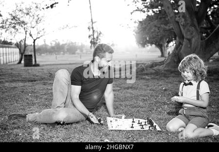 Vater und Sohn spielen Schach auf Gras im Sommerpark, Vaterschaft Stockfoto