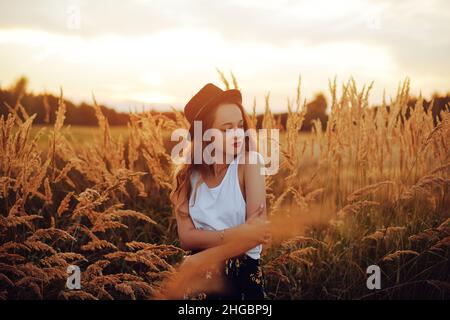 Schönheit Mädchen im Freien genießen Natur. Hübsches Teenage-Modell im Hut, das auf dem Spring Field läuft, Sun Light. Romantisches junges blondes Mädchen in einem Weizenfeld Stockfoto