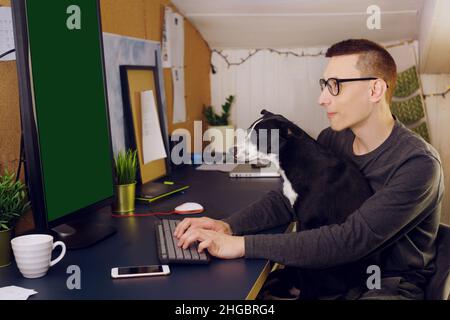 Bleiben Sie zu Hause, ein Mann sitzt zu Hause an einem Computer, ein Hund stört die Arbeit. Ein Mann arbeitet zu Hause, der Hund sitzt in seinen Armen und schaut auf den Computer. C Stockfoto