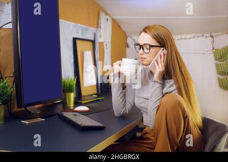 Bleiben Sie zu Hause, ein schickes Mädchen arbeitet in einer heimeligen Atmosphäre. Mädchen Freiberuflerin arbeitet an einem Computer mit Brille, Blick auf einen grünen Bildschirm auf einem Computer. Der Stockfoto