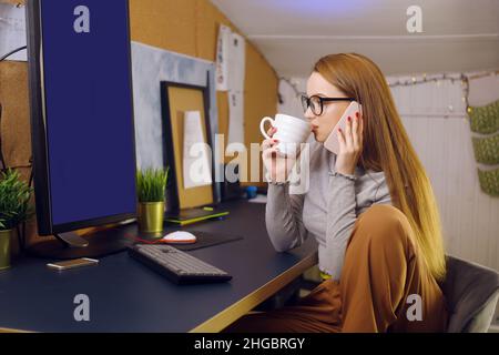 Bleiben Sie zu Hause, ein schickes Mädchen arbeitet in einer heimeligen Atmosphäre. Mädchen Freiberuflerin arbeitet an einem Computer mit Brille, Blick auf einen grünen Bildschirm auf einem Computer. Der Stockfoto