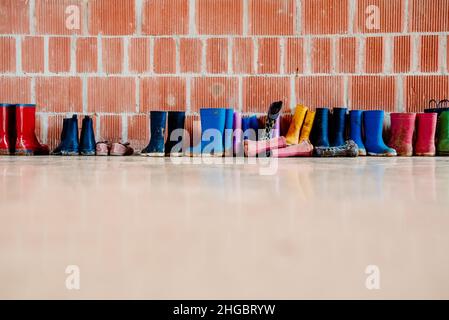 Viele schlammige farbige Gummistiefel auf dem Boden. Stockfoto