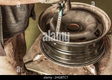 Mann, der ein Ventil in ein Rad setzt, das er in einer schmutzigen Garage repariert Stockfoto