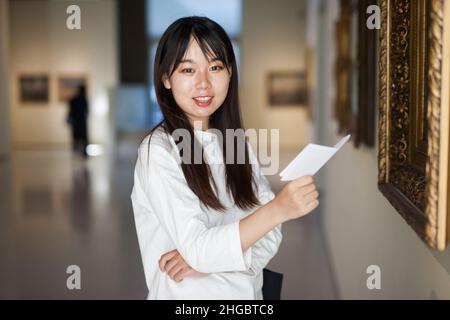 Chinesische Besucherin mit einem Reiseführer, der sich die Kunstmalerei ansieht Stockfoto