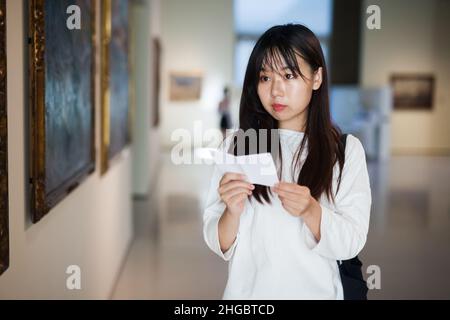 Chinesische Frau, die mit einem Reiseführer in der Nähe der Malerei in Baguette steht Stockfoto