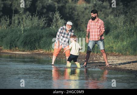 Großvater, Sohn und Enkel werfen einen Stein und Spaß am Fluss. Familiengeneration: Zukunftstraum und Menschenkonzept. Männliche Familie Mit Mehreren Generationen Stockfoto