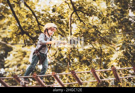 Balancieren von Balken- und Seilbrücken. Gehen Sie Ape Adventure. Kinderkonzept. Kletterer Kind beim Training. Porträt eines schönen Kindes auf einem Seilpark unter Bäumen Stockfoto