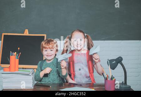 Zurück in die Schule und glückliche Zeit. Lustige kleine Kind Spaß auf Tafel Hintergrund. Freundliches Kind im Klassenzimmer spielt mit Papierflugzeug in der Nähe Stockfoto