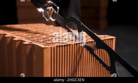 Nahaufnahme der elektrischen Schneidemaschine für kleine Keramikblöcke, die den Schneidprozess beginnen. Der Arbeiter schneidet Keramikblöcke mit einer automatischen Säge. Stockfoto