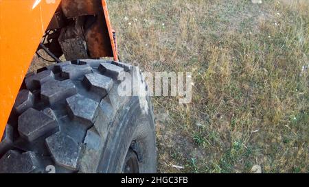 Blick von einem schweren Lastwagen, der sich auf einer verwelkten Graswiese bewegt. Nahaufnahme des großen Rades des roten Baggers, der auf dem Herbstfeld anhält. Stockfoto