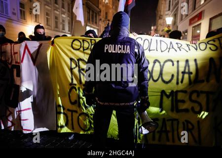 Ljubljana, Slowenien. 19th Januar 2022. Ein Polizeibeamter steht während der Demonstration mit Transparenten vor den Demonstranten. Am ersten Jahrestag der kontroversen Räumung von Künstlern und Kulturzentren aus einer besetzten alten Fahrradfabrik Rog in Ljubljana protestierten Demonstranten erneut gegen die zunehmende Privatisierung und Kommerzialisierung des öffentlichen Raums und die soziale Säuberung der Stadt, die die Bürger, vor allem die mit geringem Einkommen, aus der Stadt drängen. Kredit: SOPA Images Limited/Alamy Live Nachrichten Stockfoto