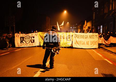 Ljubljana, Slowenien. 19th Januar 2022. Ein Polizeibeamter steht während der Demonstration mit Transparenten vor den Demonstranten. Am ersten Jahrestag der kontroversen Räumung von Künstlern und Kulturzentren aus einer besetzten alten Fahrradfabrik Rog in Ljubljana protestierten Demonstranten erneut gegen die zunehmende Privatisierung und Kommerzialisierung des öffentlichen Raums und die soziale Säuberung der Stadt, die die Bürger, vor allem die mit geringem Einkommen, aus der Stadt drängen. Kredit: SOPA Images Limited/Alamy Live Nachrichten Stockfoto