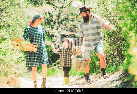 Glückliche Familie im Garten. Farmars Paar mit Sohn genießen die Natur des Frühlings und kümmern sich um ihre Pflanzen. Familie, die gemeinsam durch den geernteten Frühling geht Stockfoto