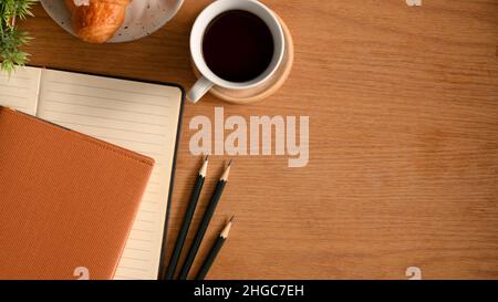 Overhead-Aufnahme eines Studientischs mit Heften, Bleistiften, Kaffee und Kopierfläche auf Holzhintergrund. Stockfoto
