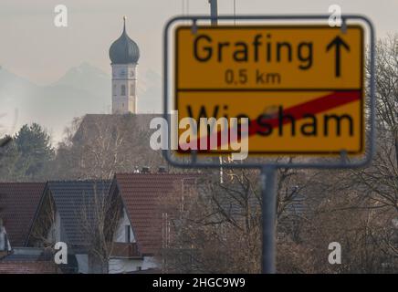 Grafing, Deutschland. 13th Januar 2022. Die katholische Kirche St. Ägidius ragt hinter dem Ortsschild von Grafing in den Himmel. Eine vom Bistum München beauftragte Kanzlei will dort am 20. Januar 2022 ein Gutachten zu Missbrauchsfällen vorlegen. Es wird sich auch um den Fall eines Priesters handeln, der der Pfarrei in der Pfarrei in der Region von Archling an der Alz zugeteilt wurde, obwohl er zuvor wegen Kindesmissbrauchs verurteilt worden war. Nach Angaben der Diözese gibt es Hinweise darauf, dass er auch in der Diözese in der Auflehnung war. Kredit: Peter Kneffel/dpa/Alamy Live Nachrichten Stockfoto