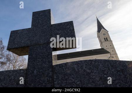 In Der Stadt, Deutschland. 13th Januar 2022. Das Kreuz eines Grabsteins erhebt sich in den Himmel vor der katholischen Kirche St. Nikolaus. Eine vom Bistum München beauftragte Kanzlei will dort am 20. Januar 2022 ein Gutachten zu Missbrauchsfällen vorlegen. Hier wird es auch um den Fall eines Priesters gehen, der in der Pfarrei in der Pfarrei in der Gemeinde von Archling an der Alz ernannt wurde, obwohl er zuvor wegen Kindesmissbrauchs verurteilt worden war. Nach Angaben der Diözese gibt es Hinweise darauf, dass er auch in der Diözese in der Auflehnung war. Kredit: Peter Kneffel/dpa/Alamy Live Nachrichten Stockfoto