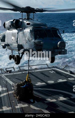 PAZIFISCHER OZEAN (Jan 17, 2022) Boatswain’s Mate Seaman Lissa Herrera, aus Hackensack, N.J., Und Boatswains Mate Seaman Bobby J. Cunningham aus Arlington, Texas, bringt einen Lastenhaken an einen MH-60R Sea Hawk-Hubschrauber an, der den „Raptors“ des Helicopter Maritime Strike Squadron (HSM) 71 zugewiesen wurde, während einer vertikalen Nachschubübung an Bord des Arleigh Burke-Klasse-Lenkraketen-Zerstörers USS Gridley (DDG 101). Die Abraham Lincoln Strike Group ist im geplanten Einsatzbereich der US-Flotte für 7th im Einsatz, um die Interoperabilität durch Allianzen und Partnerschaften zu verbessern und gleichzeitig als bereit- Stockfoto