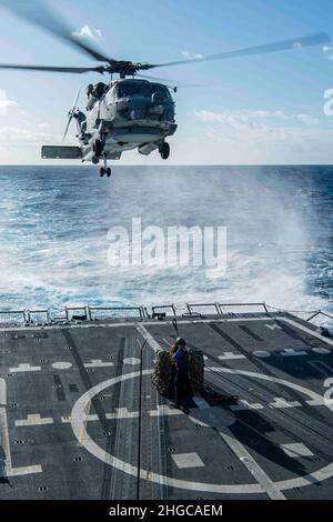 PAZIFISCHER OZEAN (Jan 17, 2022) Boatswain's Mate Seaman Bobby J. Cunningham, aus Arlington, Texas, Und Boatswains Mate Seaman Lissa Herrera aus Hackensack, N.J., bereitet sich darauf vor, während einer vertikalen Nachschubübung an Bord des Arleigh Burke-Klasse-Lenkflugkörperzerstörers USS Gridley (DDG 101) einen Frachthaken an einem MH-60R Sea Hawk-Hubschrauber zu befestigen, der den „Raptors“ des Helicopter Maritime Strike Squadron (HSM) 71 zugewiesen wurde. Die Abraham Lincoln Strike Group befindet sich im geplanten Einsatzbereich der US-Flotte für 7th, um die Interoperabilität durch Allianzen und Partnerschaften zu verbessern und gleichzeitig zu dienen Stockfoto