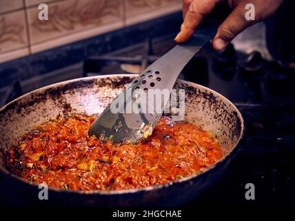 Tomatensauce mit Pilzen, Zwiebeln und Olivenöl wird in einer Pfanne auf einem Küchengasherd gebraten. Stockfoto