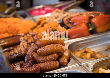 Frische leckere gegrillte und gebratene Würstchen, Gemüse und andere Speisen mit Stöcken. Street Food auf dem lokalen Markt des traditionellen Festivals. Street Food ma Stockfoto