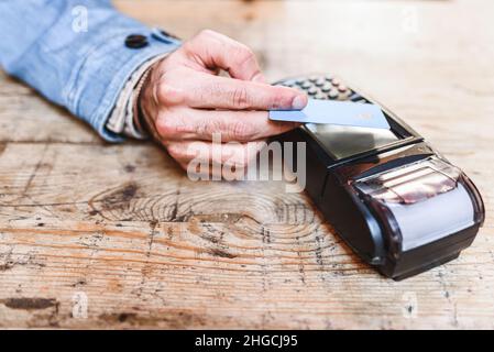 Hoher Winkel von anonymen Mann mit Kreditkarte und kontaktlosem Terminal für die Bestellung auf Holztisch im Restaurant zu bezahlen Stockfoto