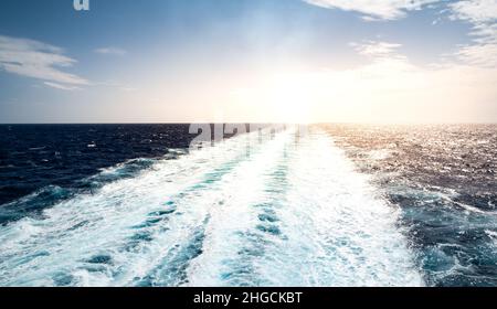 Trail im Meer von ​​a Segelkreuzfahrtschiff, das bei Sonnenuntergang wegsegelt. Stockfoto