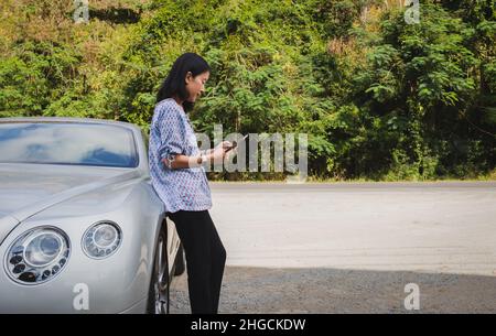 Frau, die neben dem Auto steht und versucht, das Signal auf dem Handy zu bekommen. Stockfoto