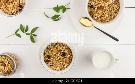 Draufsicht auf Schalen mit hausgemachtem Müsli oder Müsli aus Haferflocken, Rosinen, Nüssen mit einem Becher frischer Milch. Gesunde Ernährung Stockfoto