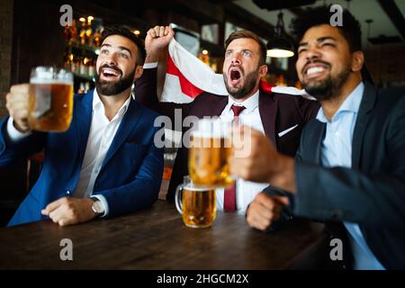 Männerfans schreien und beobachten Fußball im Fernsehen und trinken Bier in einer Kneipe Stockfoto