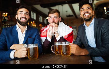 Männerfans schreien und beobachten Fußball im Fernsehen und trinken Bier in einer Kneipe Stockfoto