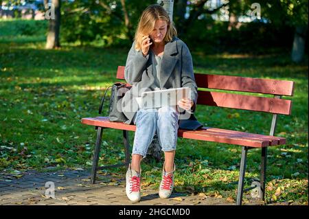 Eine Frau mit Laptop sitzt an einem sonnigen Sommertag auf einer Parkbank Stockfoto