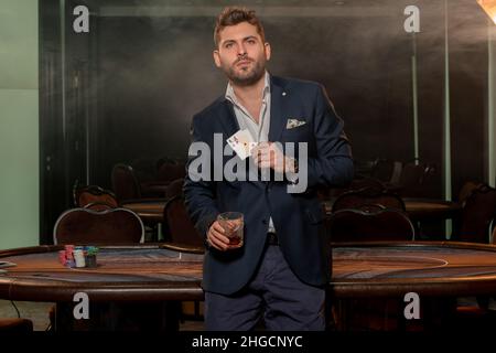 Junger Spieler mit einem Glas Getränk und einem Pokerspiel, das zwei Asse im Casino gewinnt Stockfoto