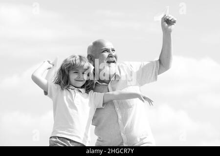 Großvater und Sohn spielen mit Spielzeug Papierflugzeug vor Sommerhimmel Hintergrund. Kleiner Junge mit Träumen vom Fliegen. Familienverhältnis Großvater und Stockfoto